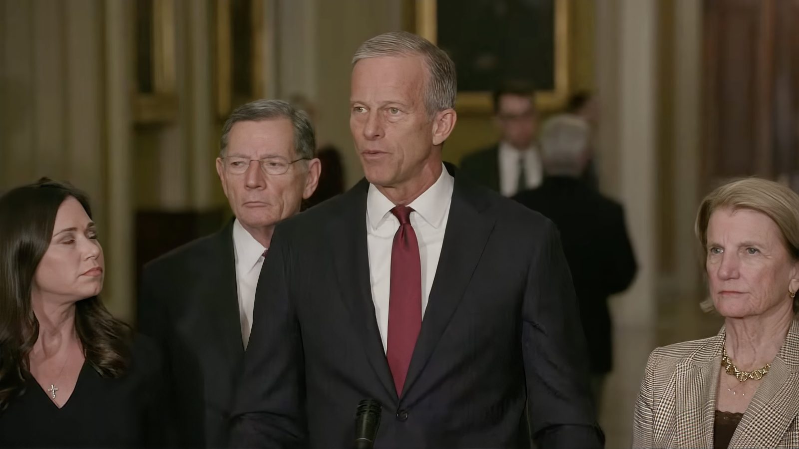 Group of four U.S. senators speaking at a press conference in a formal setting, discussing legislative issues and policy decisions.