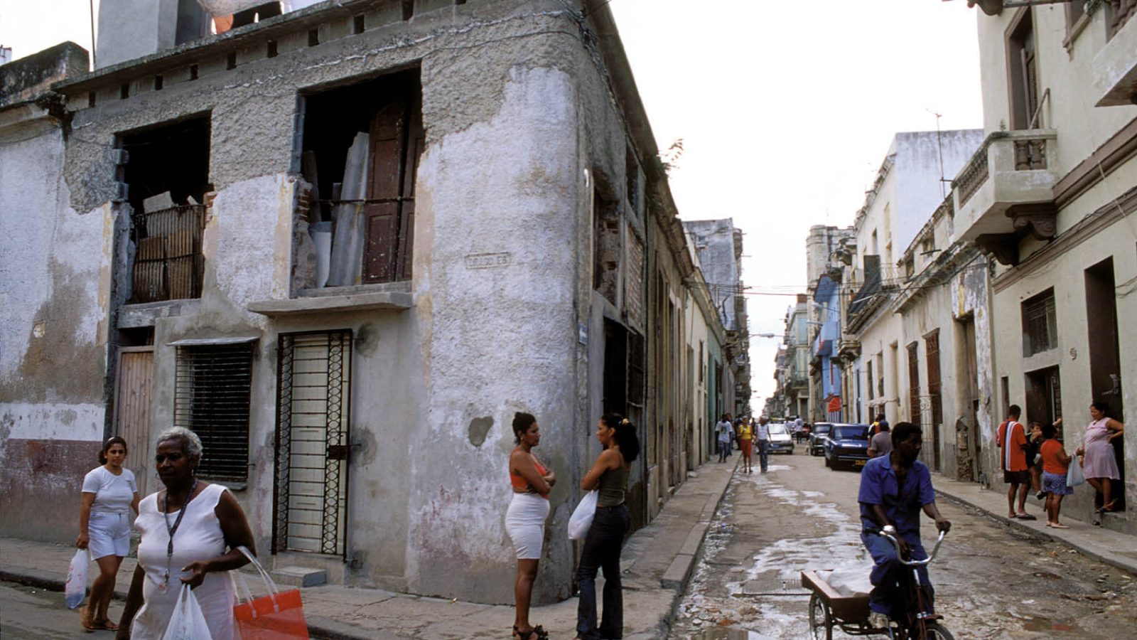 Street scene in Havana featuring pedestrians, a cyclist, and historic buildings with weathered facades, showcasing the vibrant urban life and culture of Cuba.