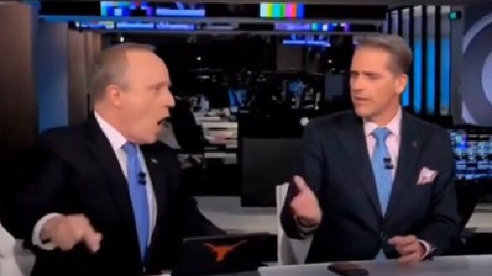 Two news anchors passionately discussing a topic on a television set, with a modern newsroom backdrop and technology visible.