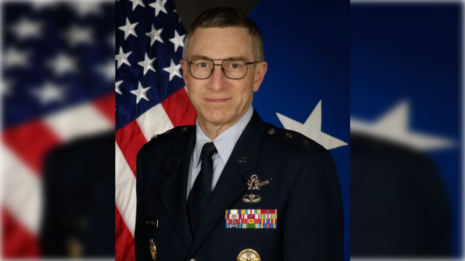 Portrait of a military officer in uniform with medals, standing in front of American flags, signifying leadership and service in the armed forces.