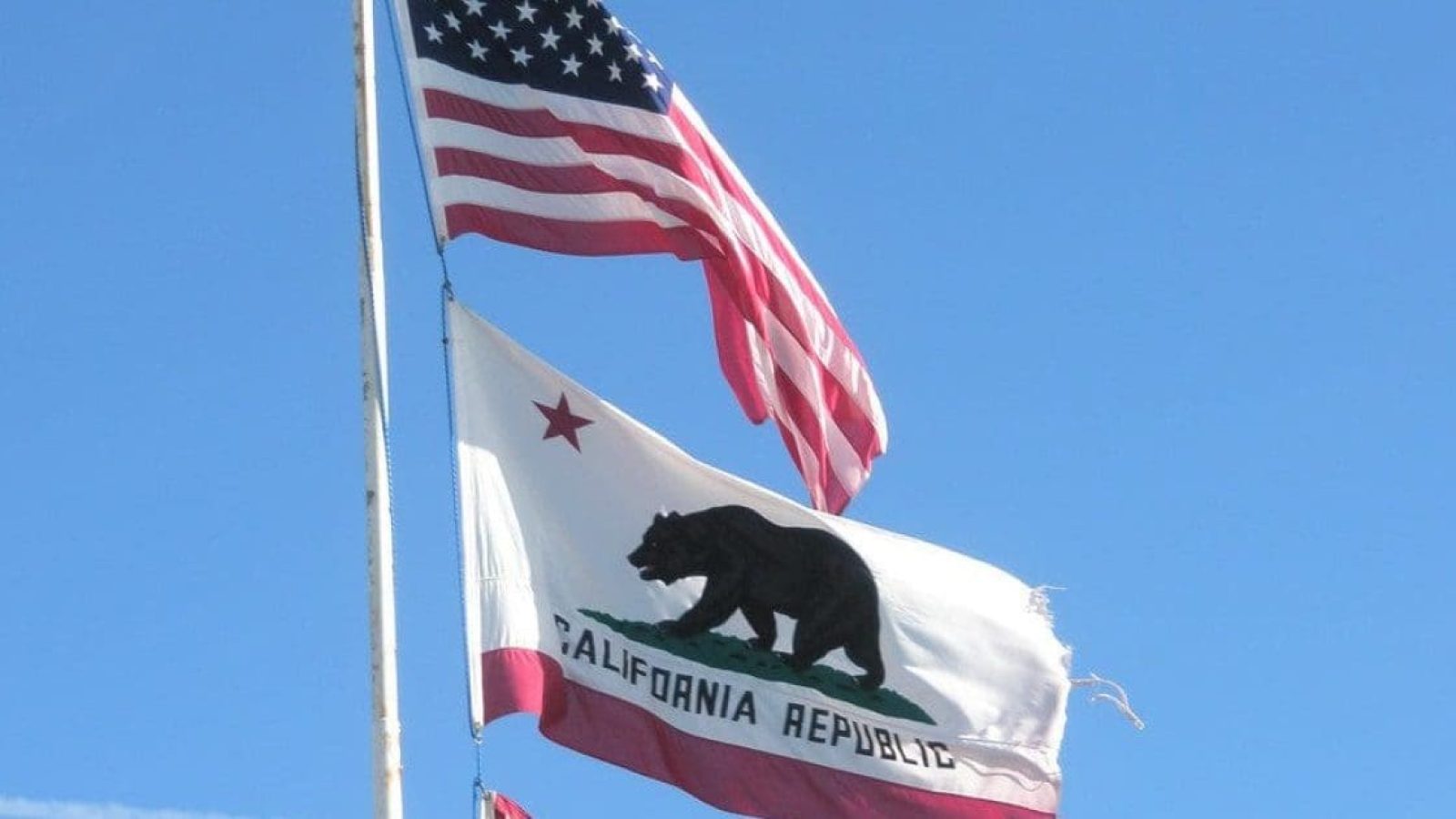 American and California flags waving against a clear blue sky, symbolizing patriotism and state pride.