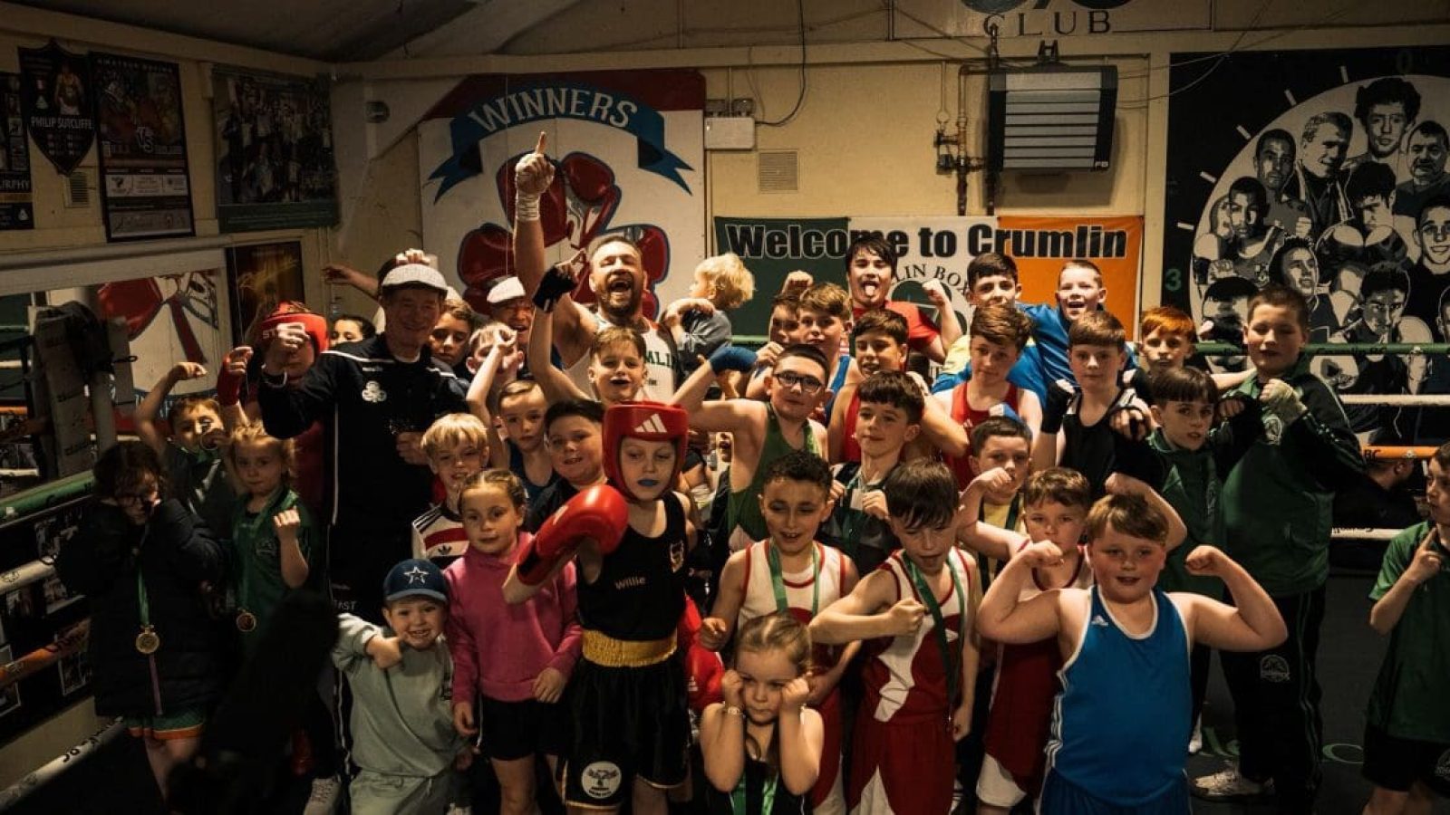 A large group of young boxers celebrating in a gym, showcasing their medals and team spirit after a successful event at Crumlin Boxing Club.
