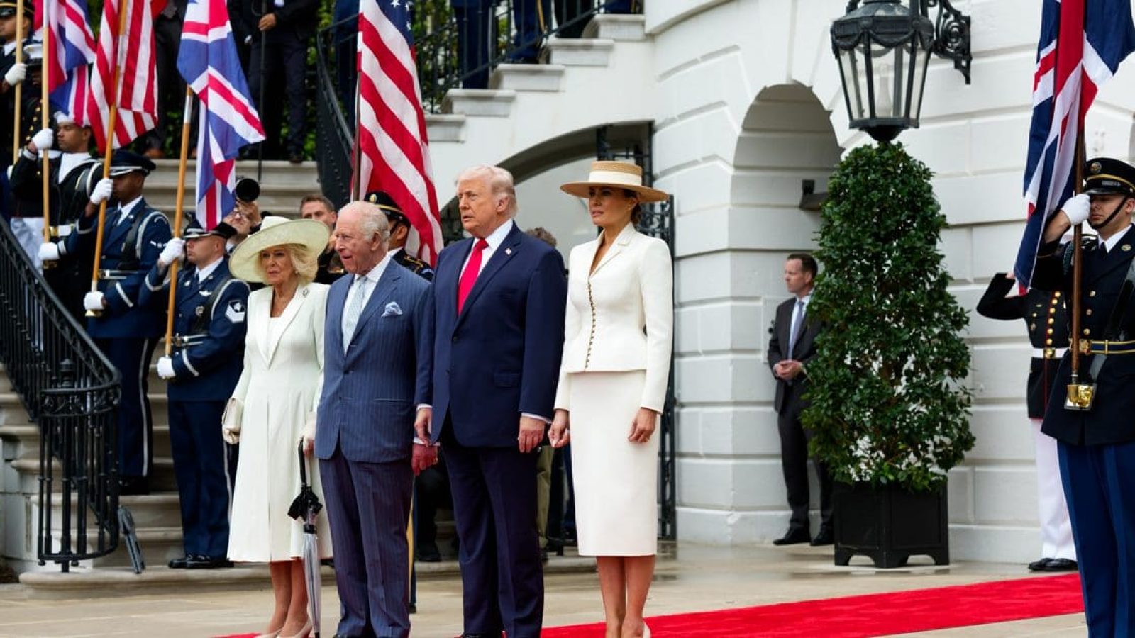World leaders including Donald Trump and King Charles III stand together at a formal event, flanked by military honor guards and flags.