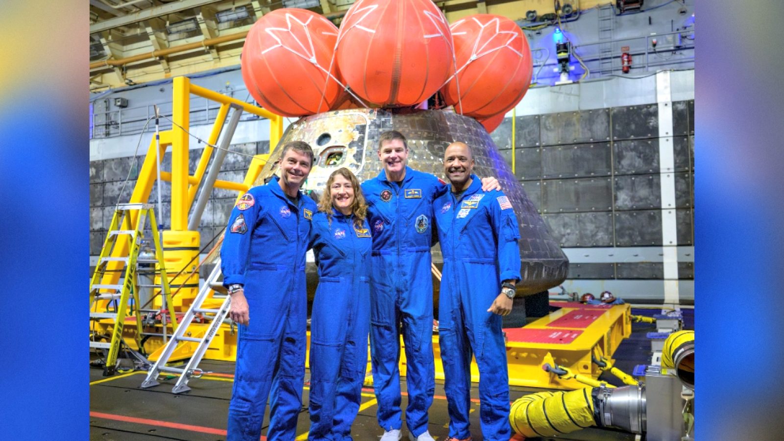Four astronauts in blue flight suits pose in front of a spacecraft with a distinctive capsule design, showcasing advancements in space exploration technology.