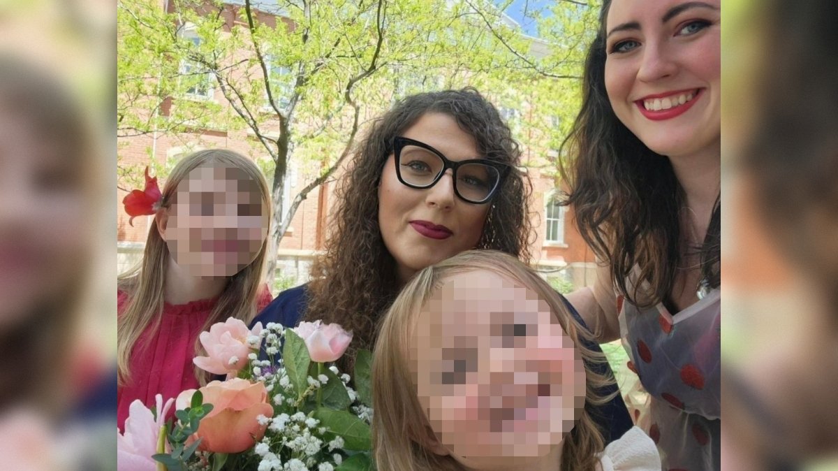 Group of smiling women and children holding a bouquet of flowers outdoors, surrounded by green trees and a sunny atmosphere.