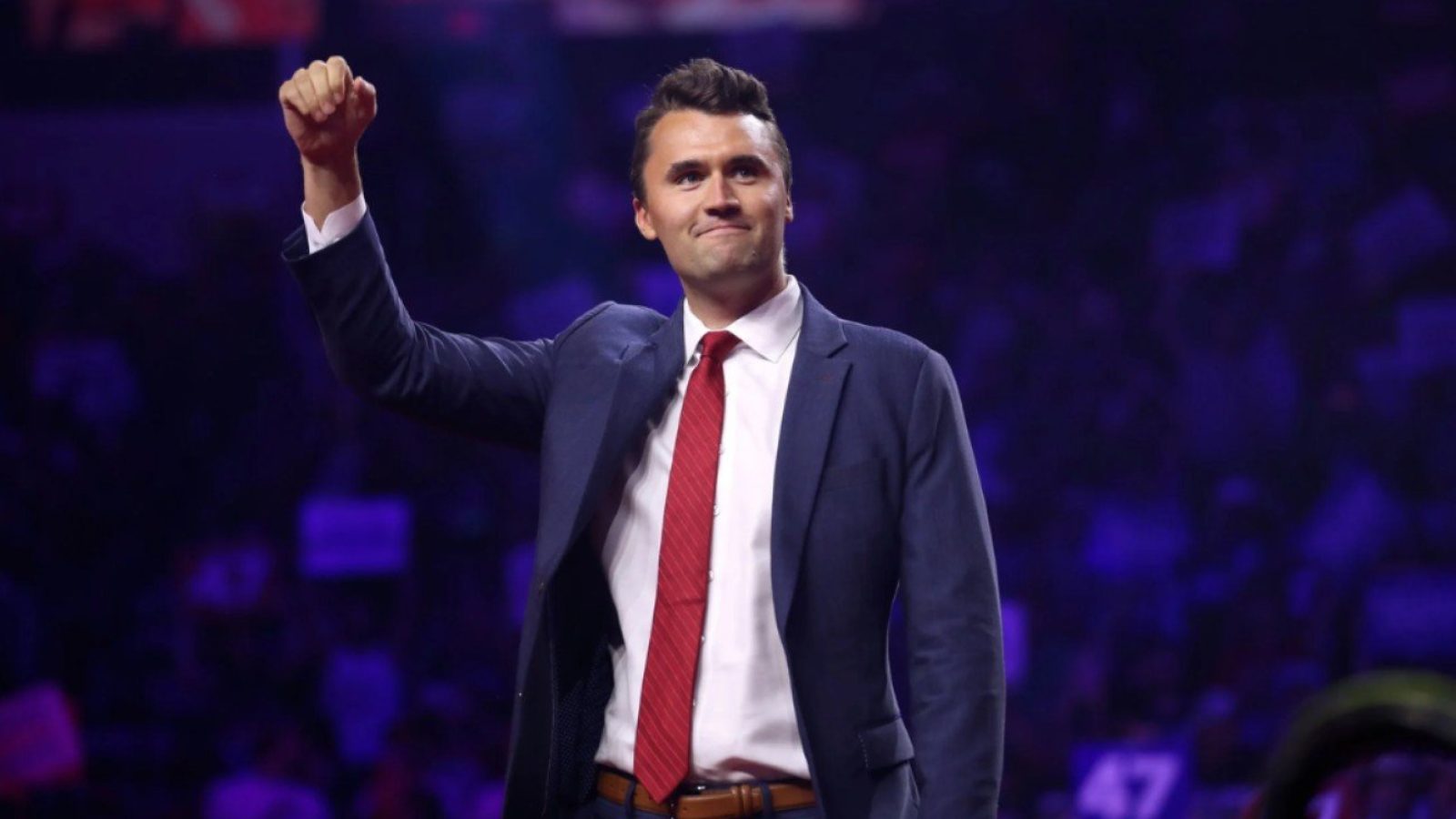 Man in a suit raising his fist in a crowd, expressing confidence and enthusiasm at a public event.