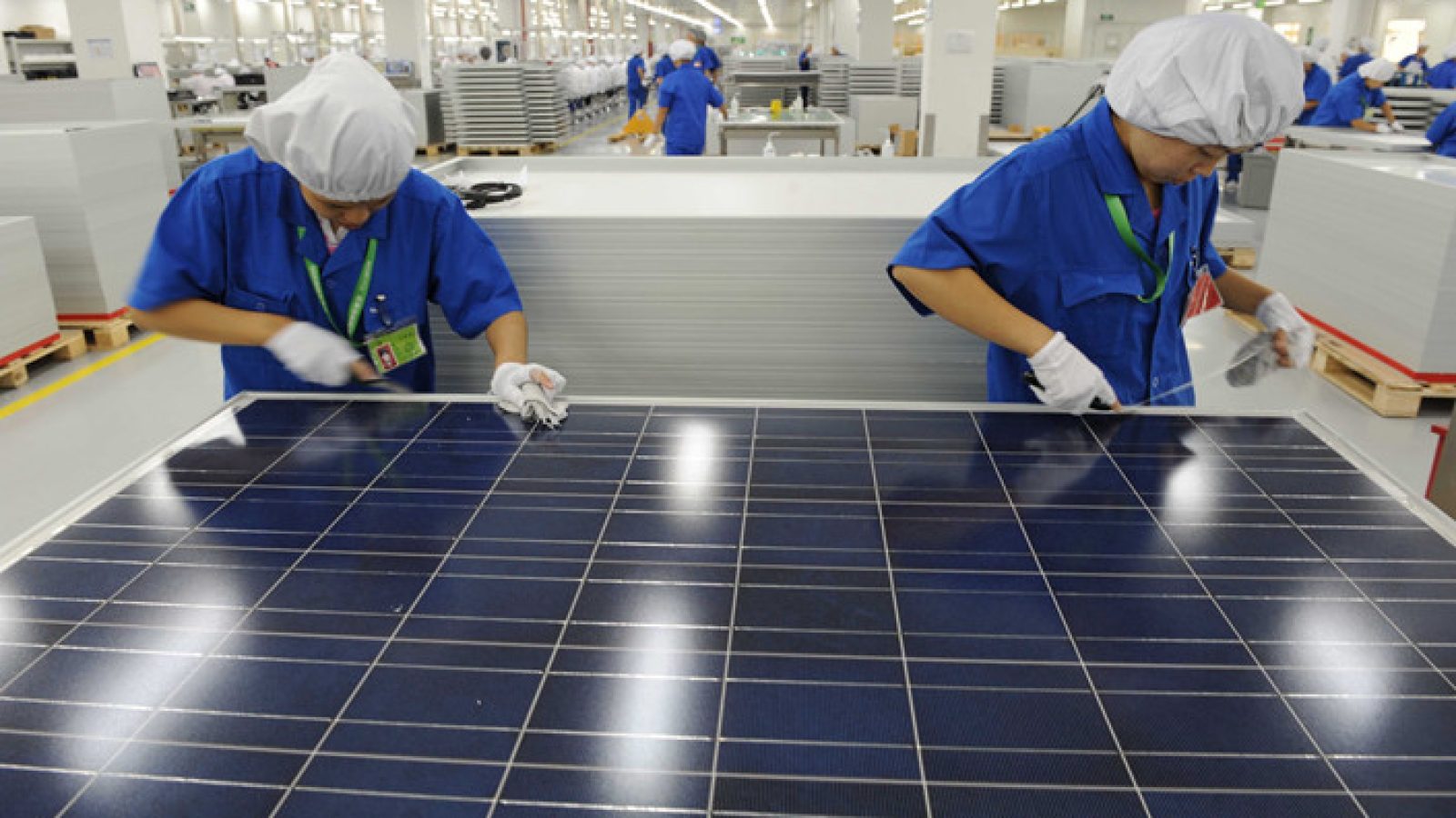 Workers in a solar panel manufacturing facility inspect and assemble photovoltaic panels on a production line.