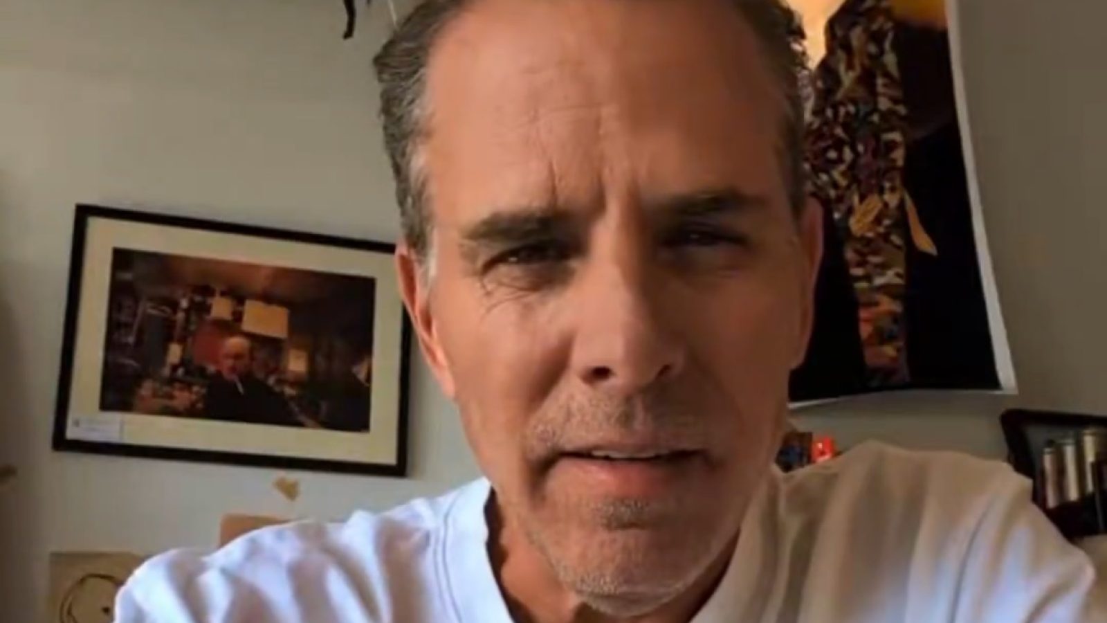 Man in a white shirt sitting in a room with art on the walls, looking directly at the camera.