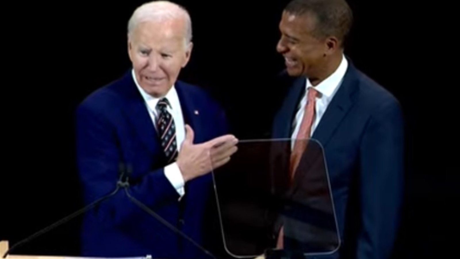 Joe Biden and a smiling associate engage in conversation at a podium during a public event, highlighting a moment of camaraderie and connection.