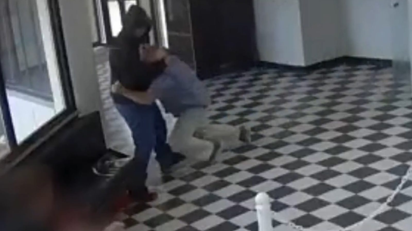 Two individuals are engaged in a physical altercation inside a building with a checkered floor and large windows.
