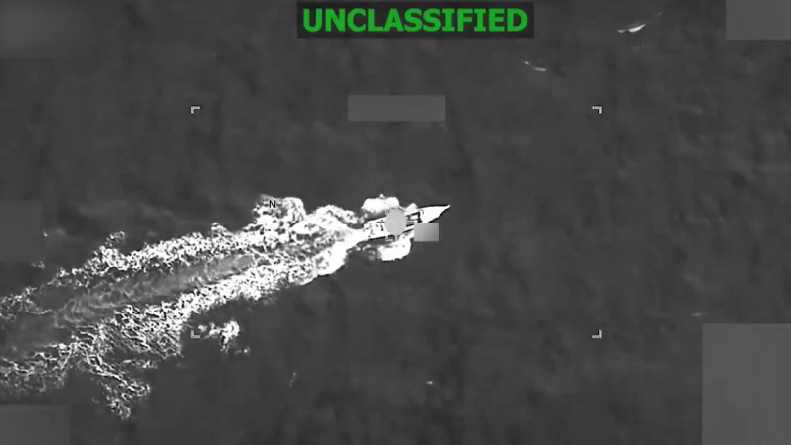 Aerial view of a boat speeding through dark ocean waters, captured in an unclassified thermal imaging format.