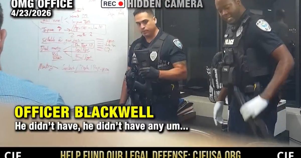 Officers in tactical gear discussing a situation in an office, with a whiteboard displaying notes and diagrams in the background.