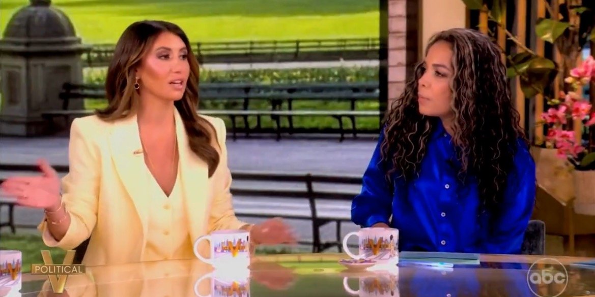 Two women engage in discussion on a talk show set, showcasing diverse opinions and lively conversation against a park backdrop.