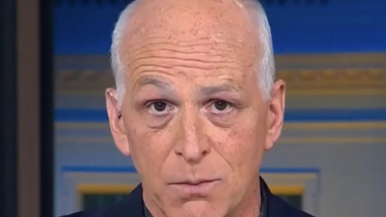 Close-up of a man with a bald head and serious expression, discussing current events in a broadcast setting.