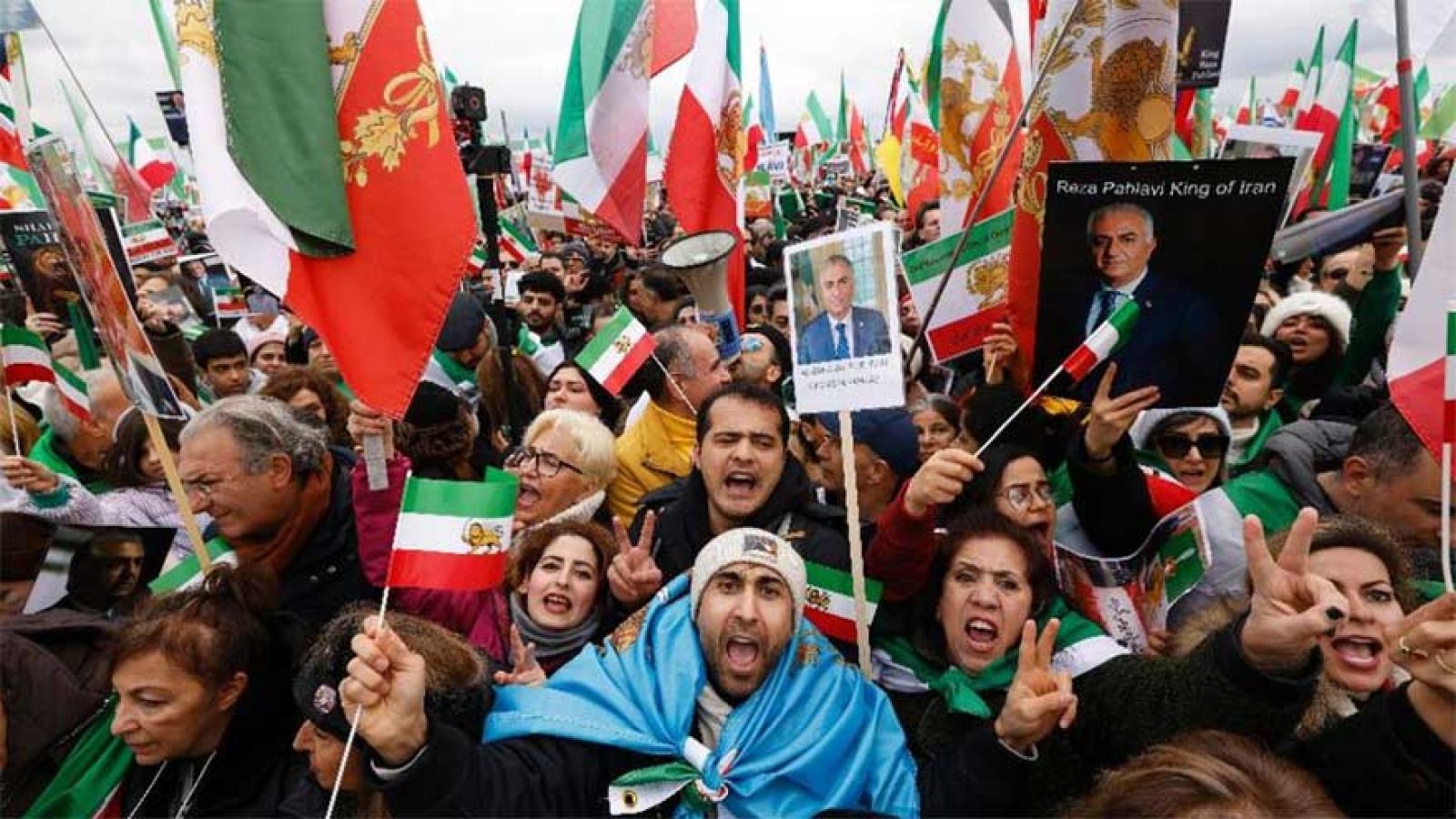 Crowd of protesters holding Iranian flags and signs during a rally advocating for political change in Iran.
