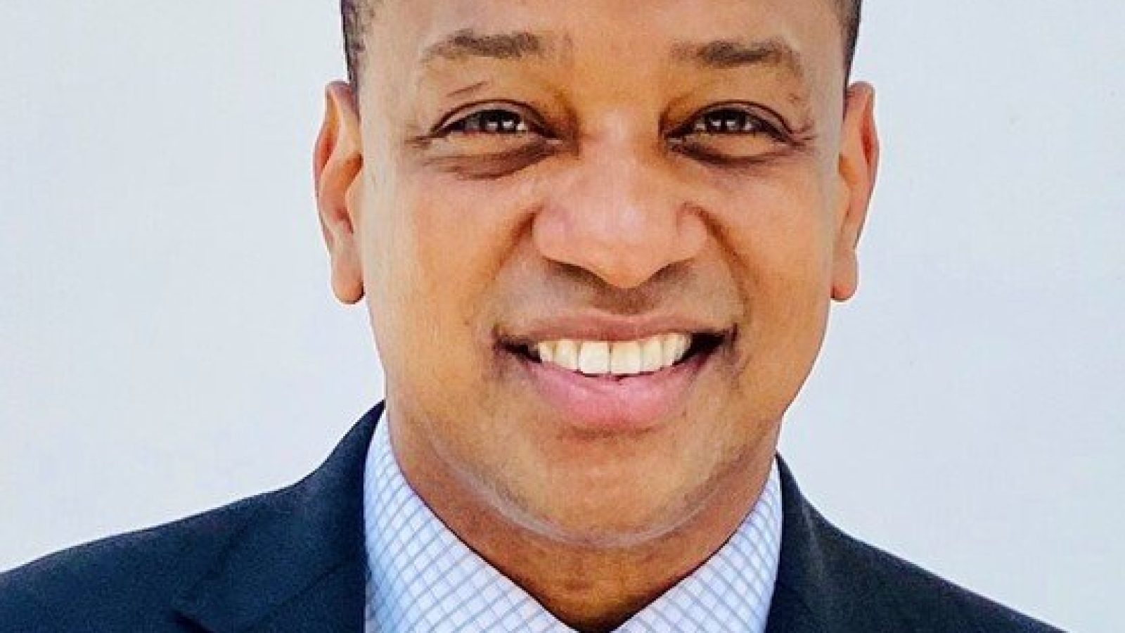 Smiling professional man in a suit with a light blue tie, against a plain white background, exuding confidence and approachability.