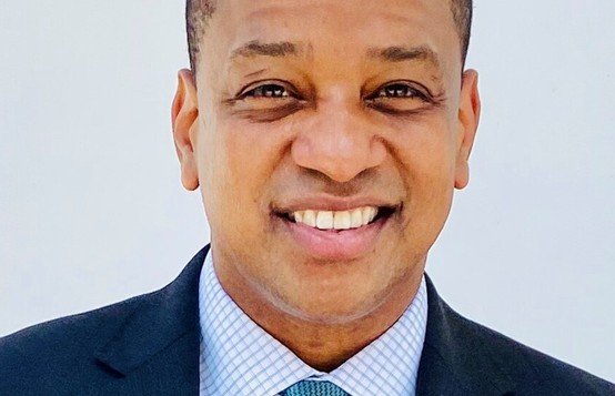 Smiling professional man in a suit with a light blue tie, against a plain white background, exuding confidence and approachability.