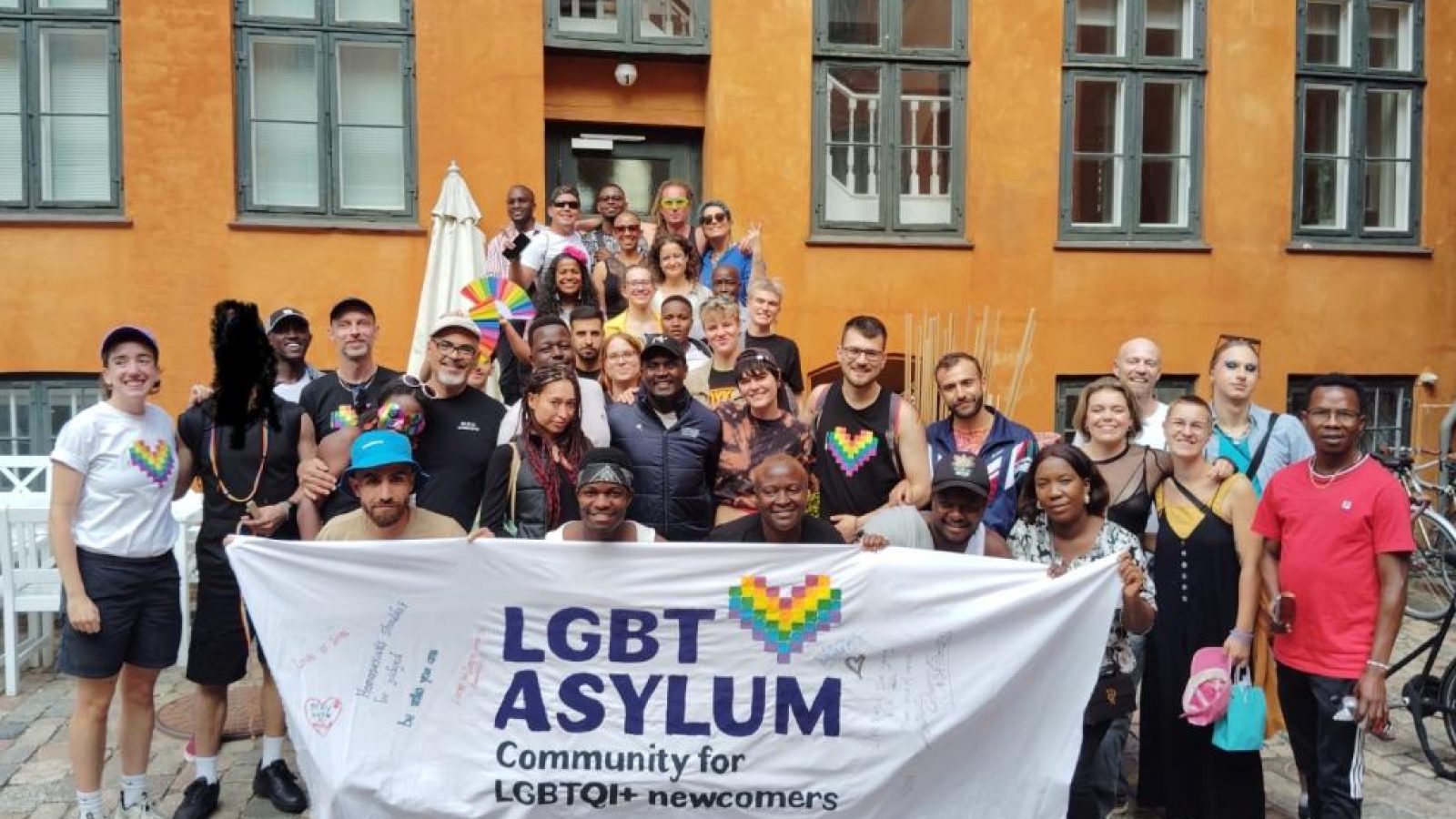 Group photo of LGBTQI+ newcomers and supporters at an event for LGBT Asylum, showcasing community and solidarity.