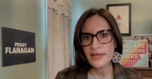 Peggy Flanagan speaks during a virtual event, with signs promoting inclusivity visible in the background.