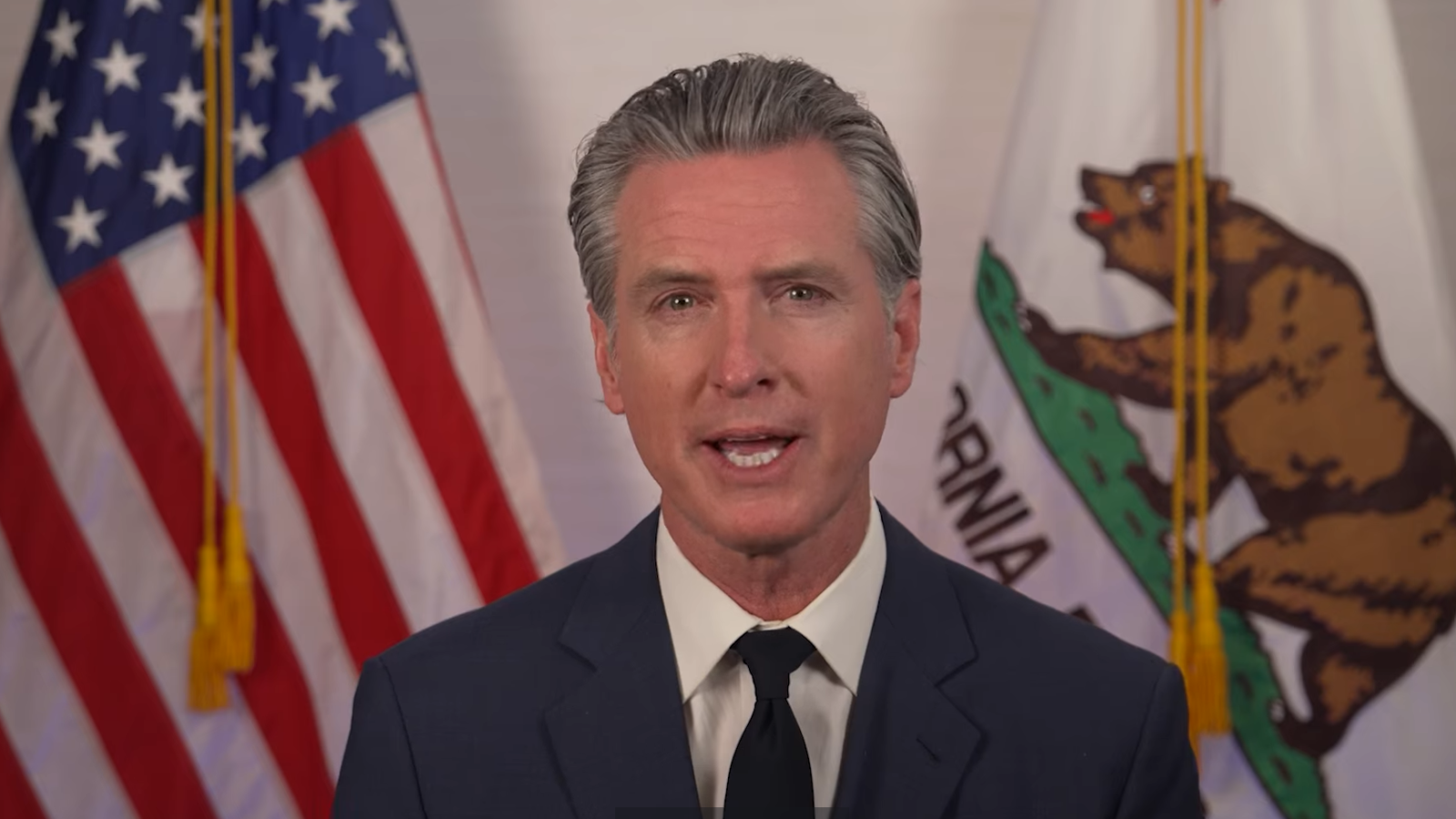 California Governor speaking in front of the American and California flags, addressing key state issues in a formal setting.