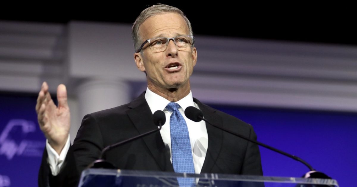 Man in a suit speaking at a podium with microphones, delivering a speech at a conference event.