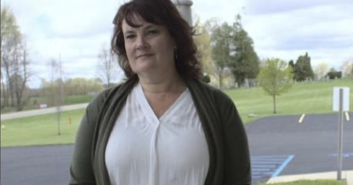 Woman standing outdoors in a green cardigan, with a blurred park background and overcast sky, conveying a calm and approachable demeanor.