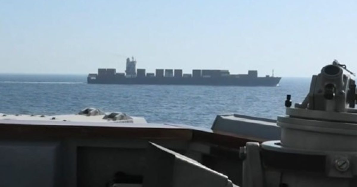 View of a large cargo ship sailing on calm waters, captured from the deck of another vessel.