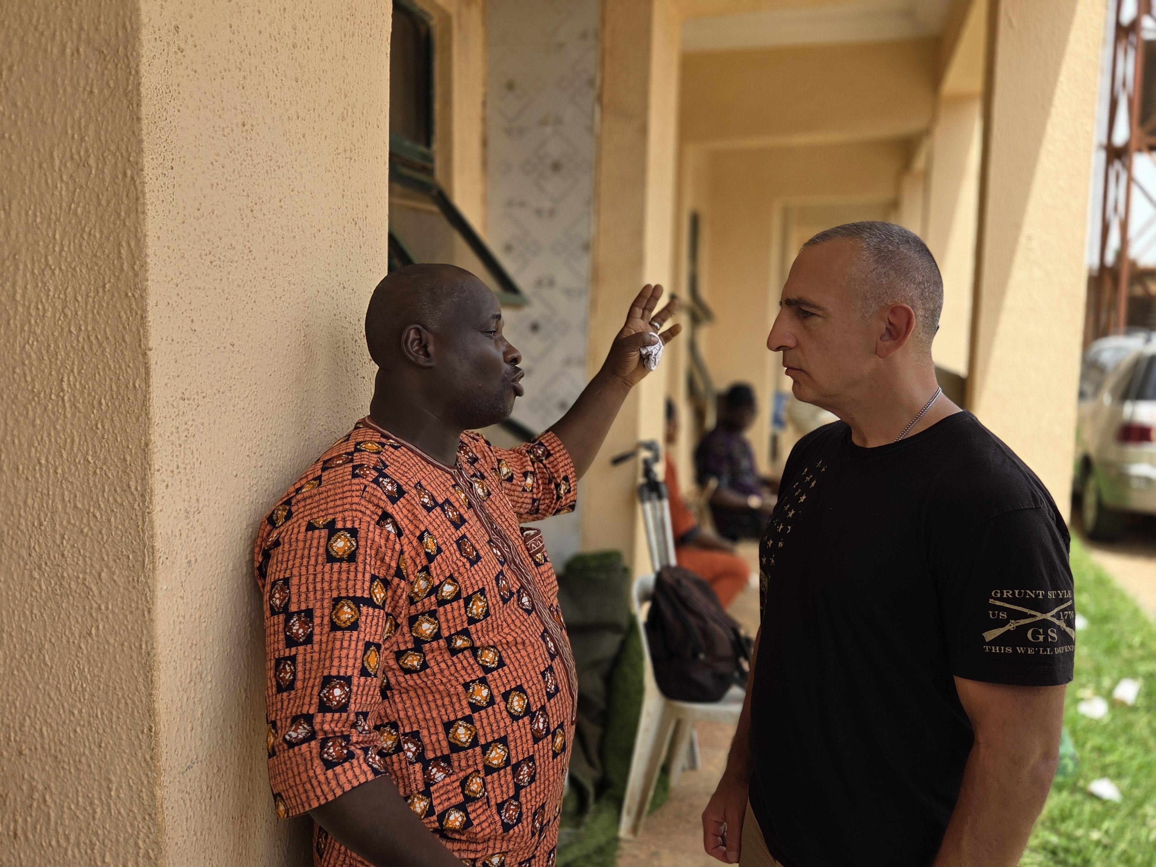 Two men engaged in a serious discussion outside a building, with one gesturing while the other listens intently.