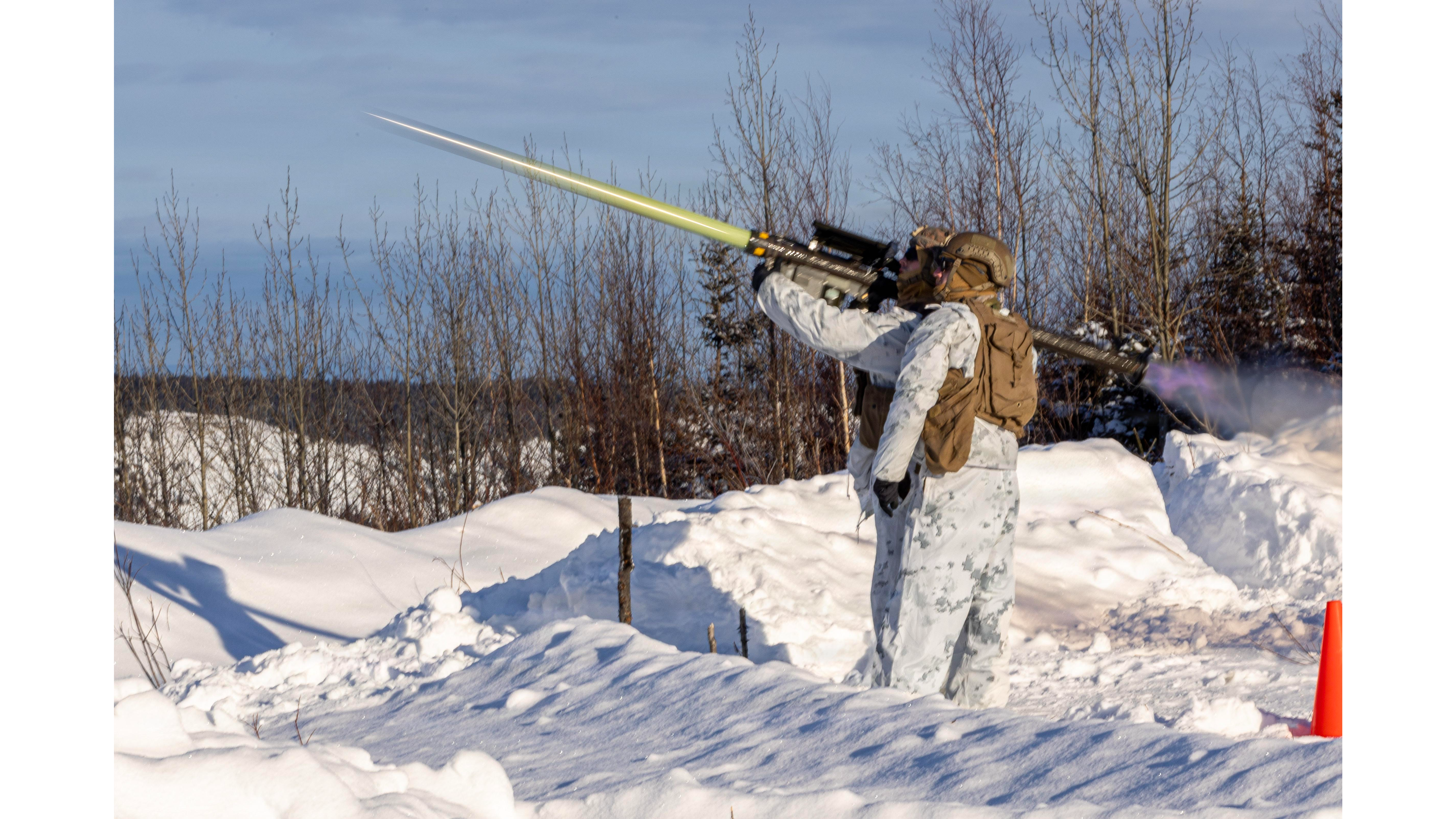 Soldier in winter camouflage firing a missile launcher in a snowy landscape, demonstrating military training and equipment usage.