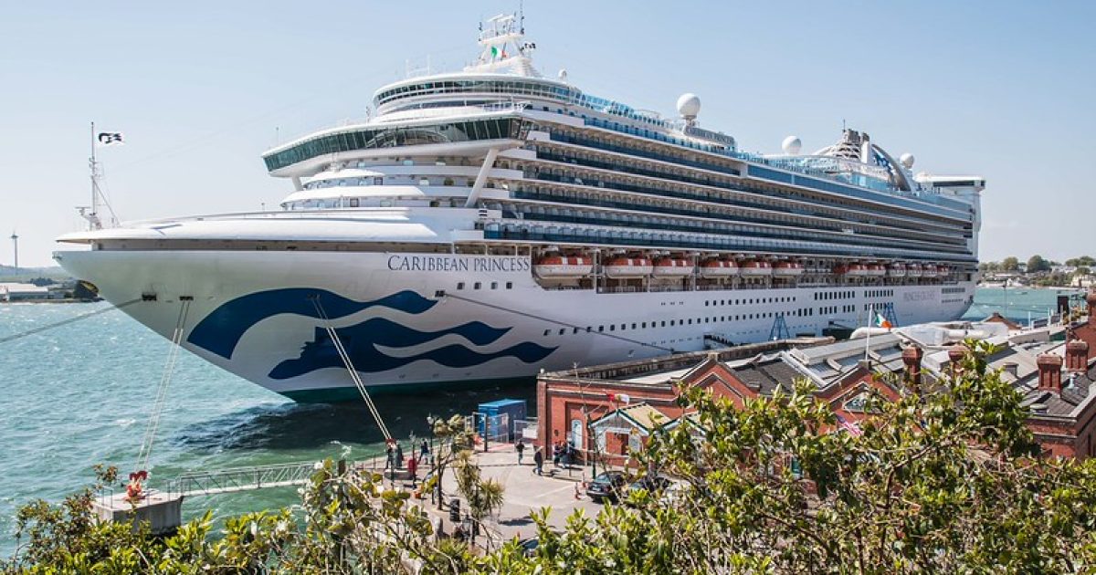 Caribbean Princess cruise ship docked near a waterfront with people and buildings visible in the foreground.