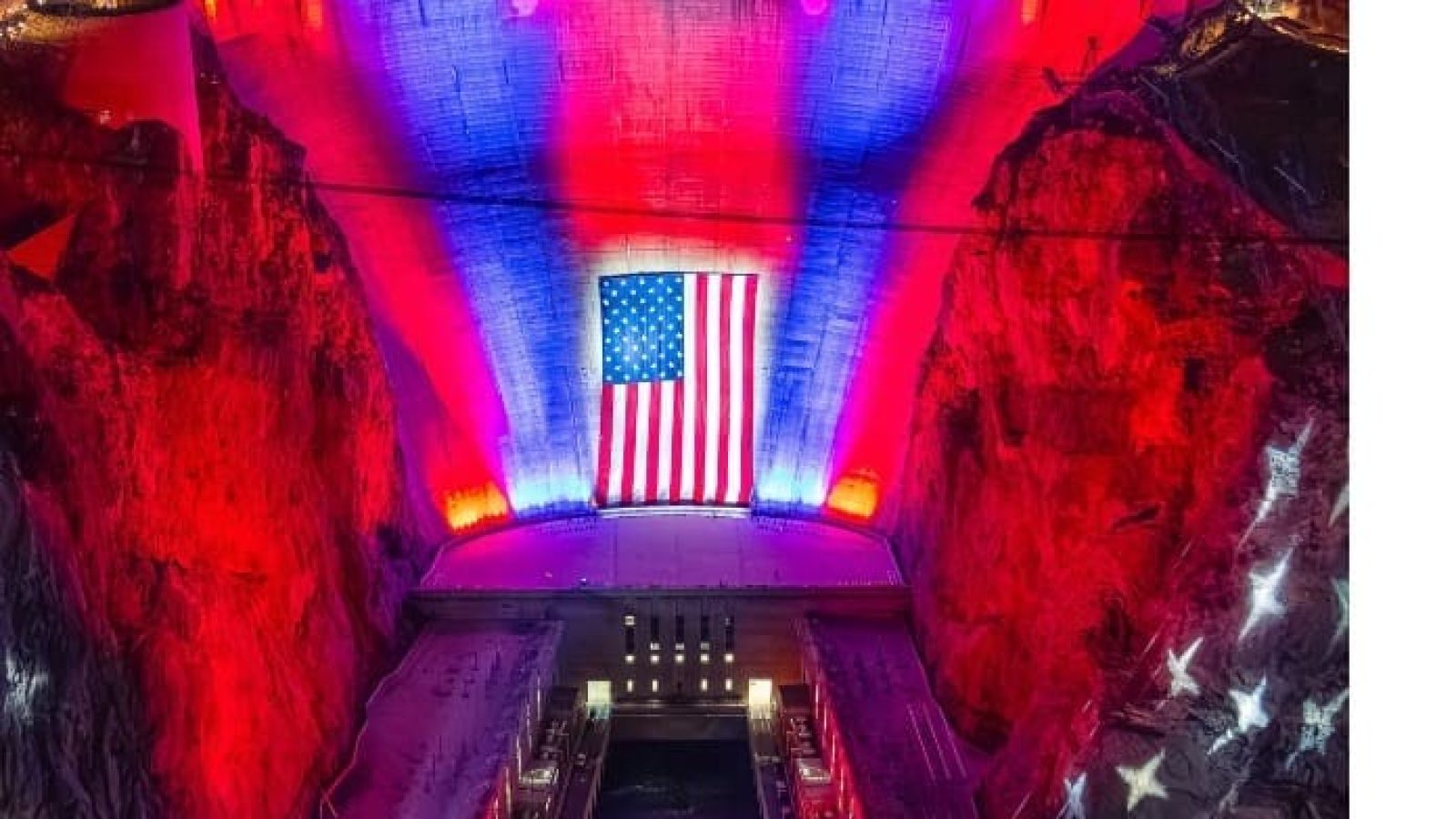Colorful lights illuminate the Hoover Dam, featuring a large American flag projection on its face, symbolizing patriotism and national pride.