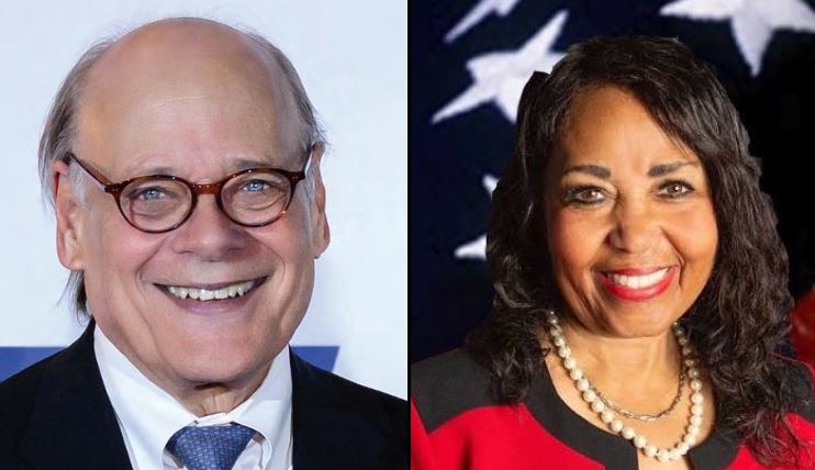 Headshots of two smiling politicians, one with glasses and a blue suit, the other with dark hair and a red outfit, set against a patriotic background.