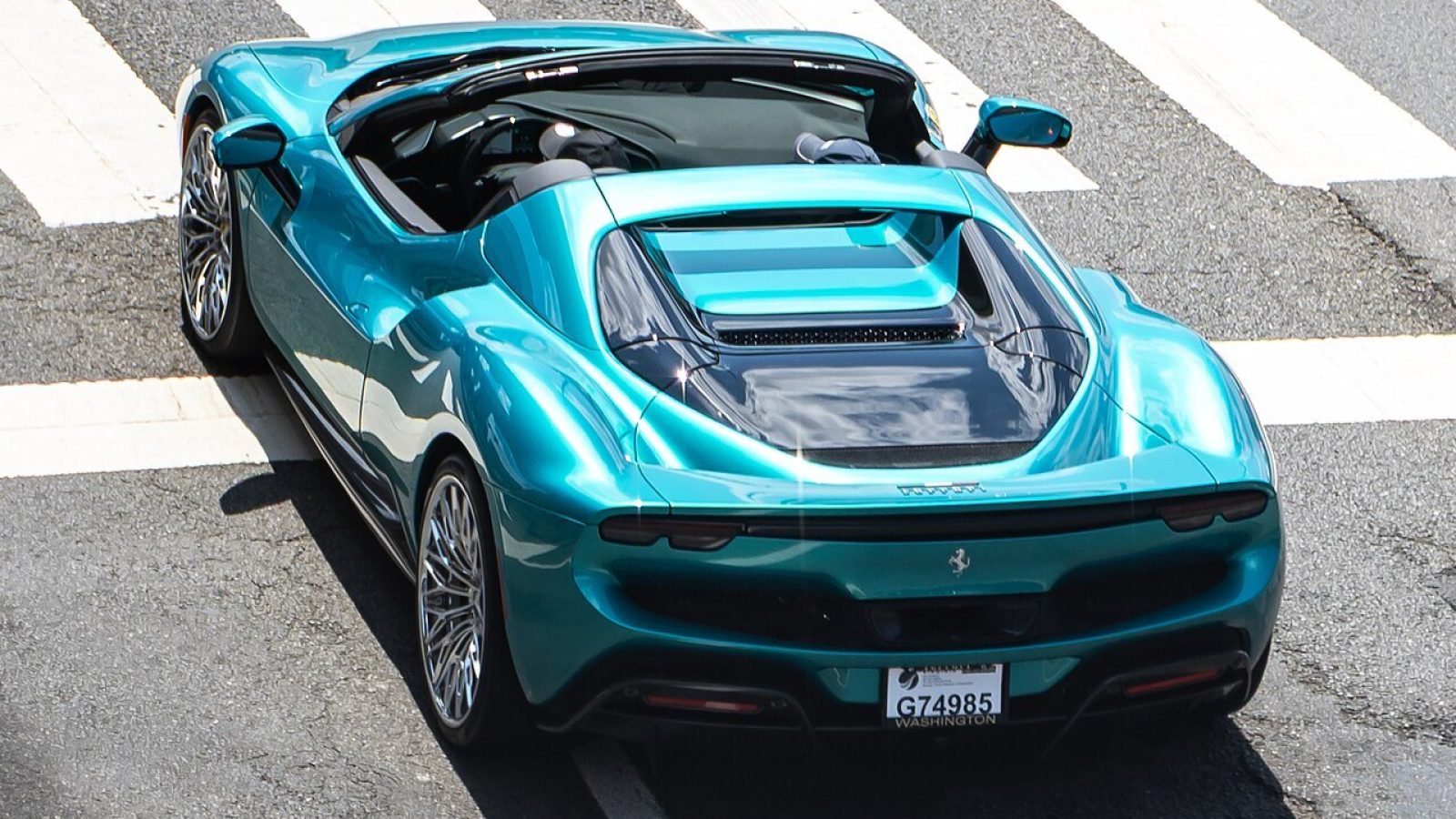 A sleek turquoise convertible sports car parked on a crosswalk, showcasing its modern design and shiny alloy wheels.