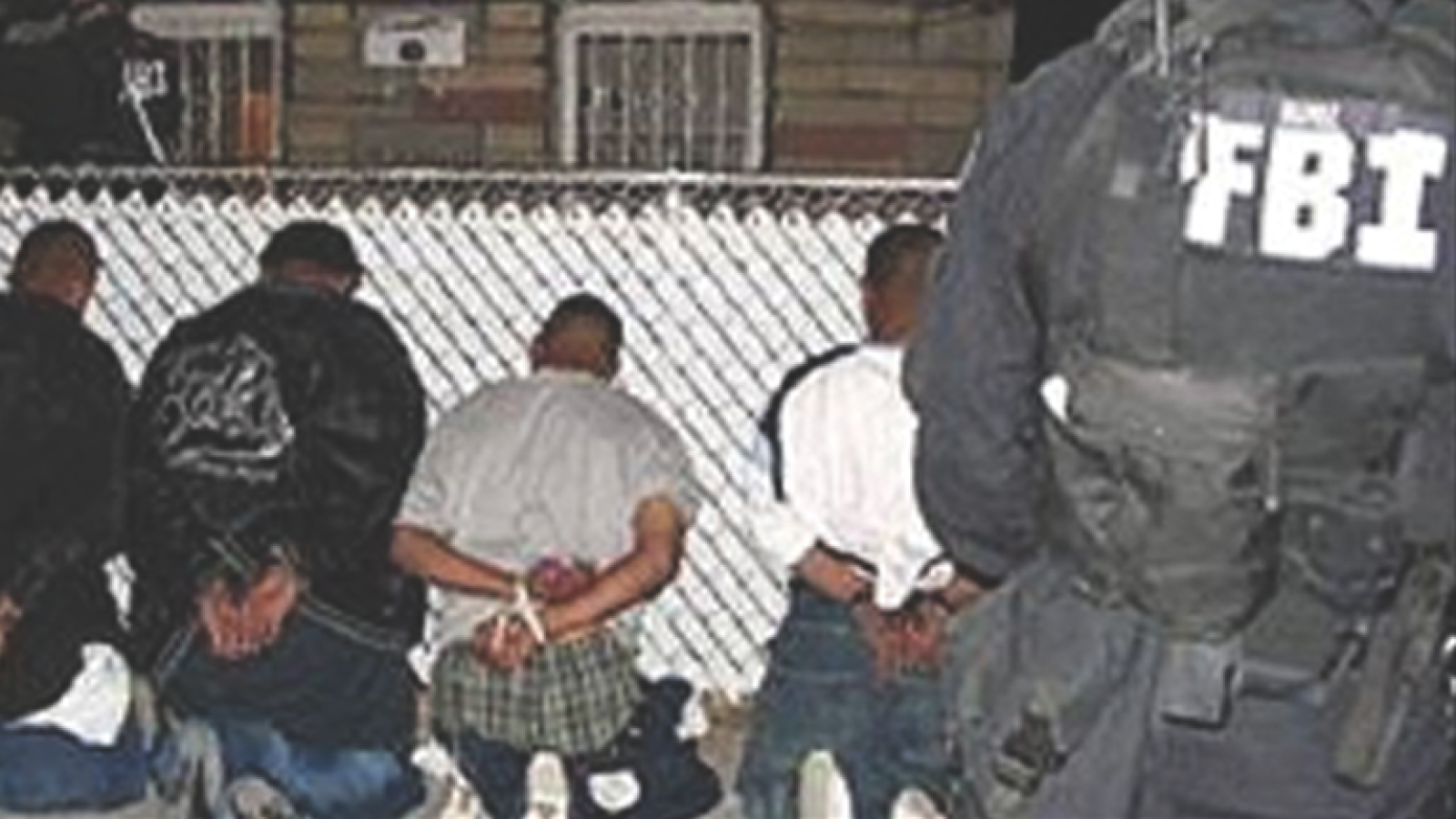 FBI agents apprehend suspects during a nighttime operation, with individuals handcuffed and seated against a fence.