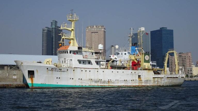 Research vessel docked in a harbor with a city skyline in the background, showcasing marine exploration and scientific study.