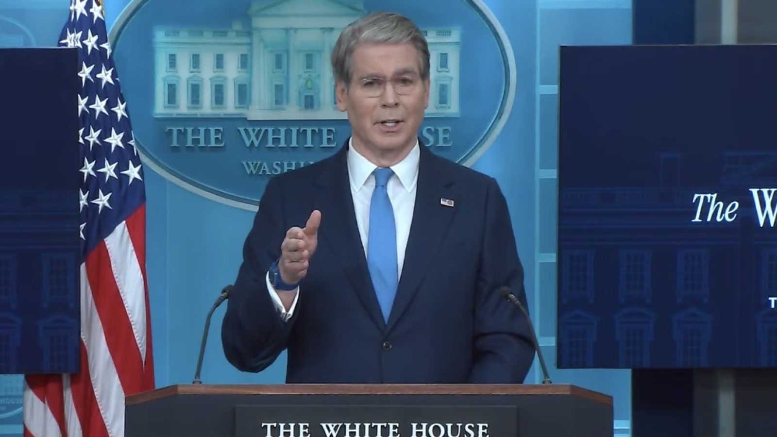 Press briefing at the White House featuring a speaker addressing the audience with an American flag in the background.