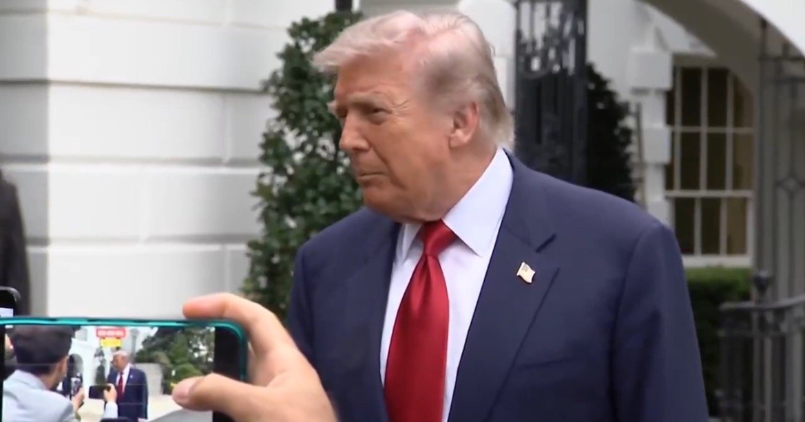 Former President Donald Trump speaking outside the White House, with a person capturing the moment on a smartphone.