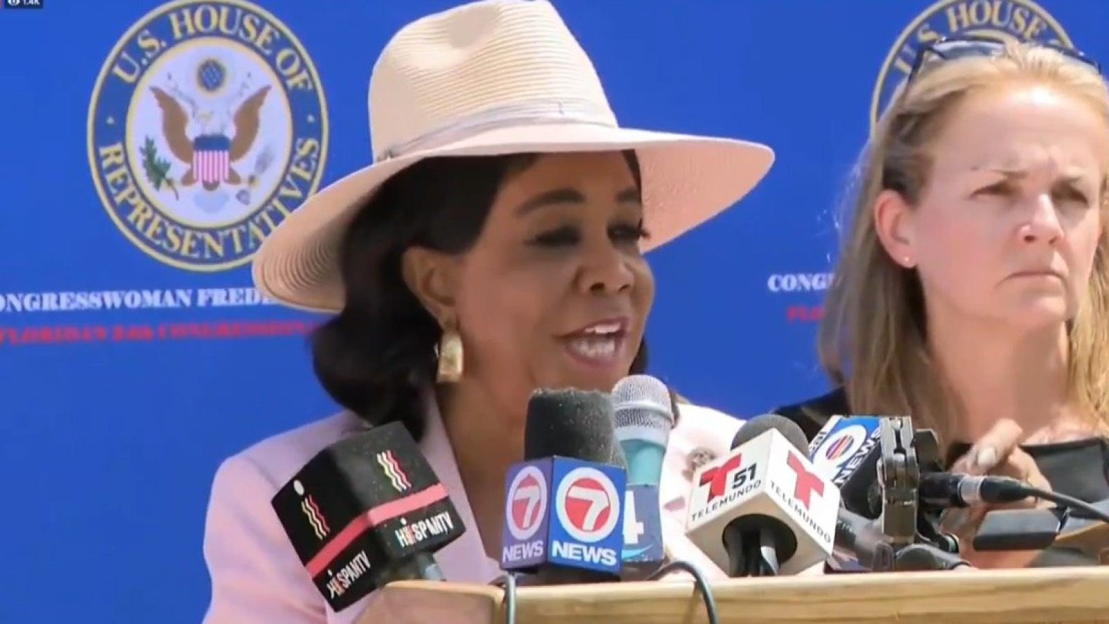 Congresswoman speaking at a press conference with various media microphones, highlighting important issues in front of a U.S. House of Representatives backdrop.