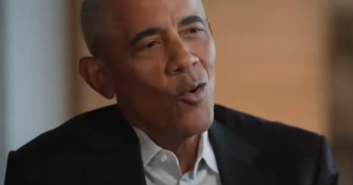 Former President Barack Obama speaking in an interview, dressed in a suit, with a thoughtful expression in a well-lit setting.