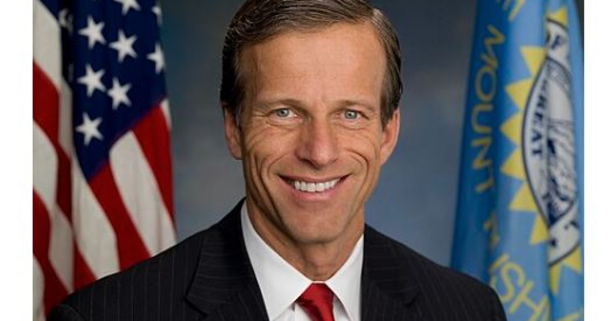 Portrait of a smiling male politician in a suit with a red tie, American flag in the background, representing leadership and public service.