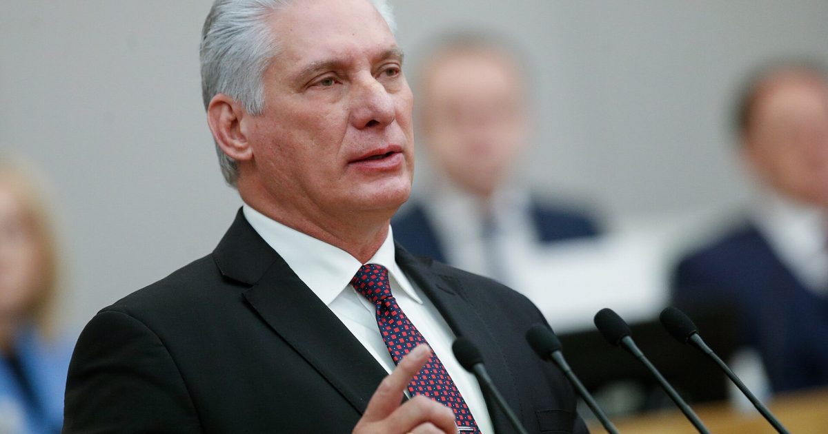 Cuban leader delivering a speech at a conference, emphasizing key points with a raised finger, dressed in a formal suit.