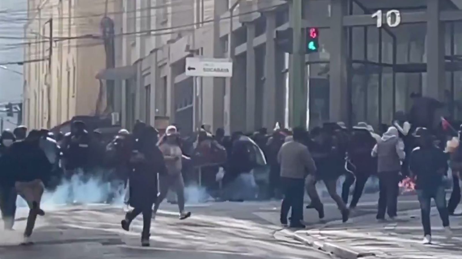 Crowd fleeing from tear gas during a protest in an urban setting, with buildings and traffic signals visible in the background.