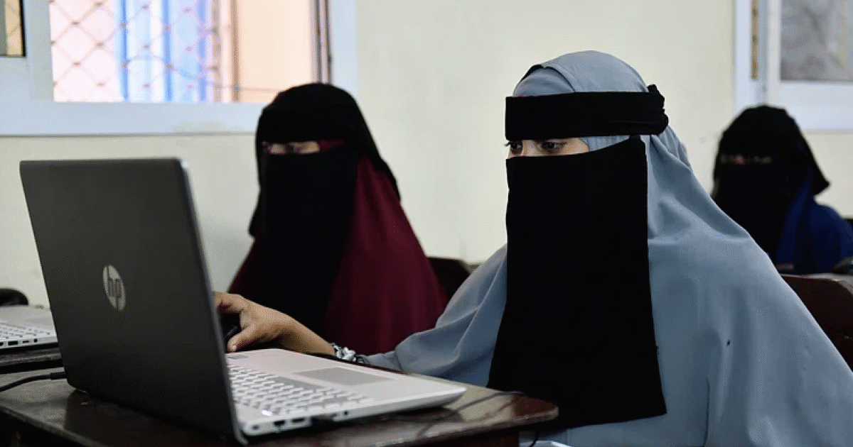 Women in traditional attire using laptops in a classroom, demonstrating engagement in technology and education.