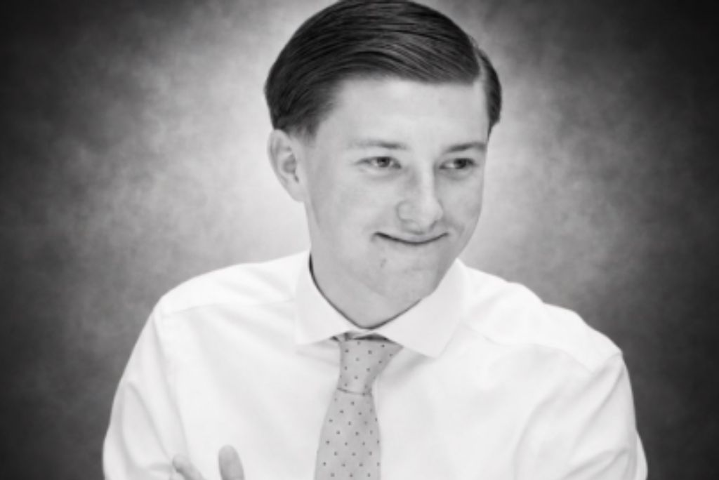 Smiling young man in a white shirt and patterned tie, captured in a black and white portrait with a soft background.