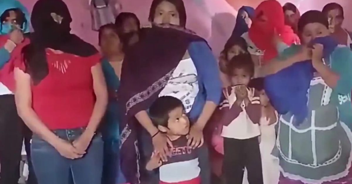 Group of women and children in a community gathering, some wearing masks and colorful shawls, highlighting cultural expressions and solidarity.