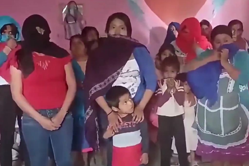 Group of women and children in a community gathering, some wearing masks and colorful shawls, highlighting cultural expressions and solidarity.