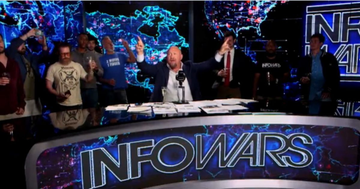 Alex Jones leads a lively discussion on the Infowars set, surrounded by enthusiastic supporters, with a digital map backdrop.