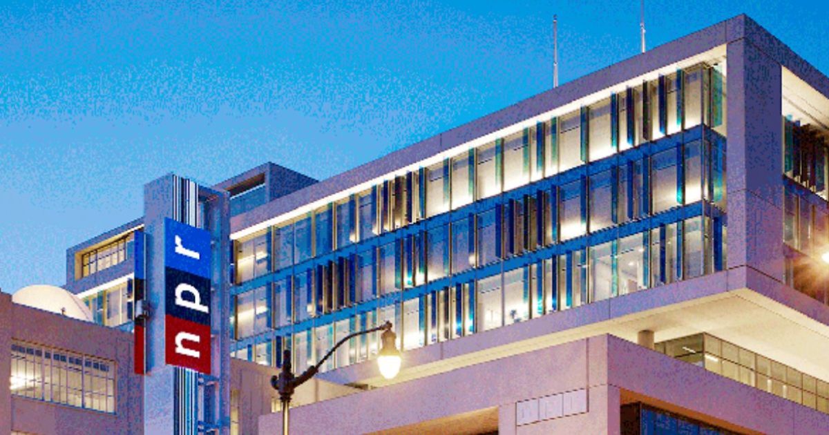 NPR headquarters building illuminated at dusk, showcasing modern architecture and the iconic NPR logo prominently displayed.