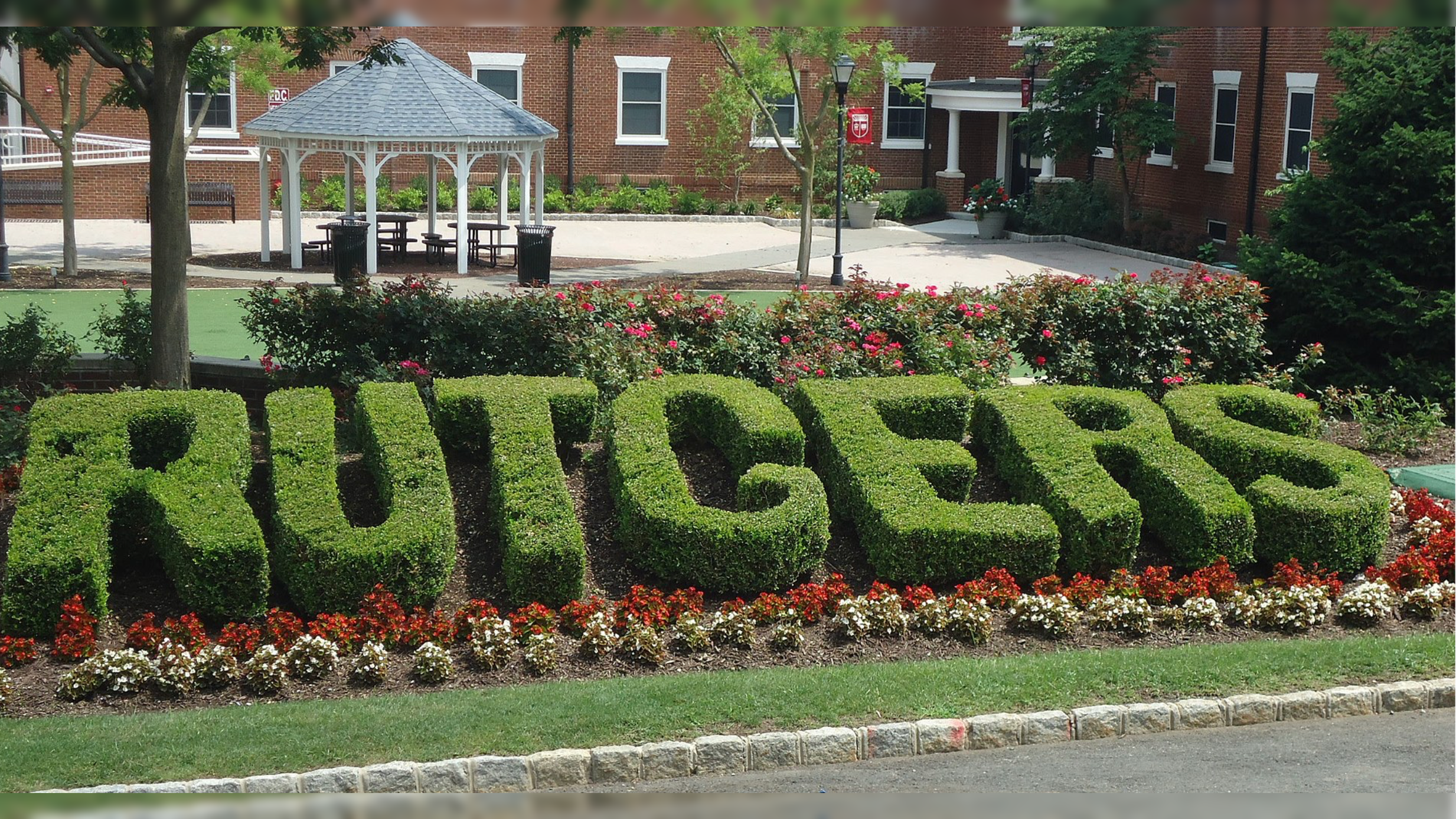 Topiary bushes spelling "Rutgers" surrounded by colorful flowers in a campus setting, showcasing the university's vibrant landscaping and outdoor spaces.