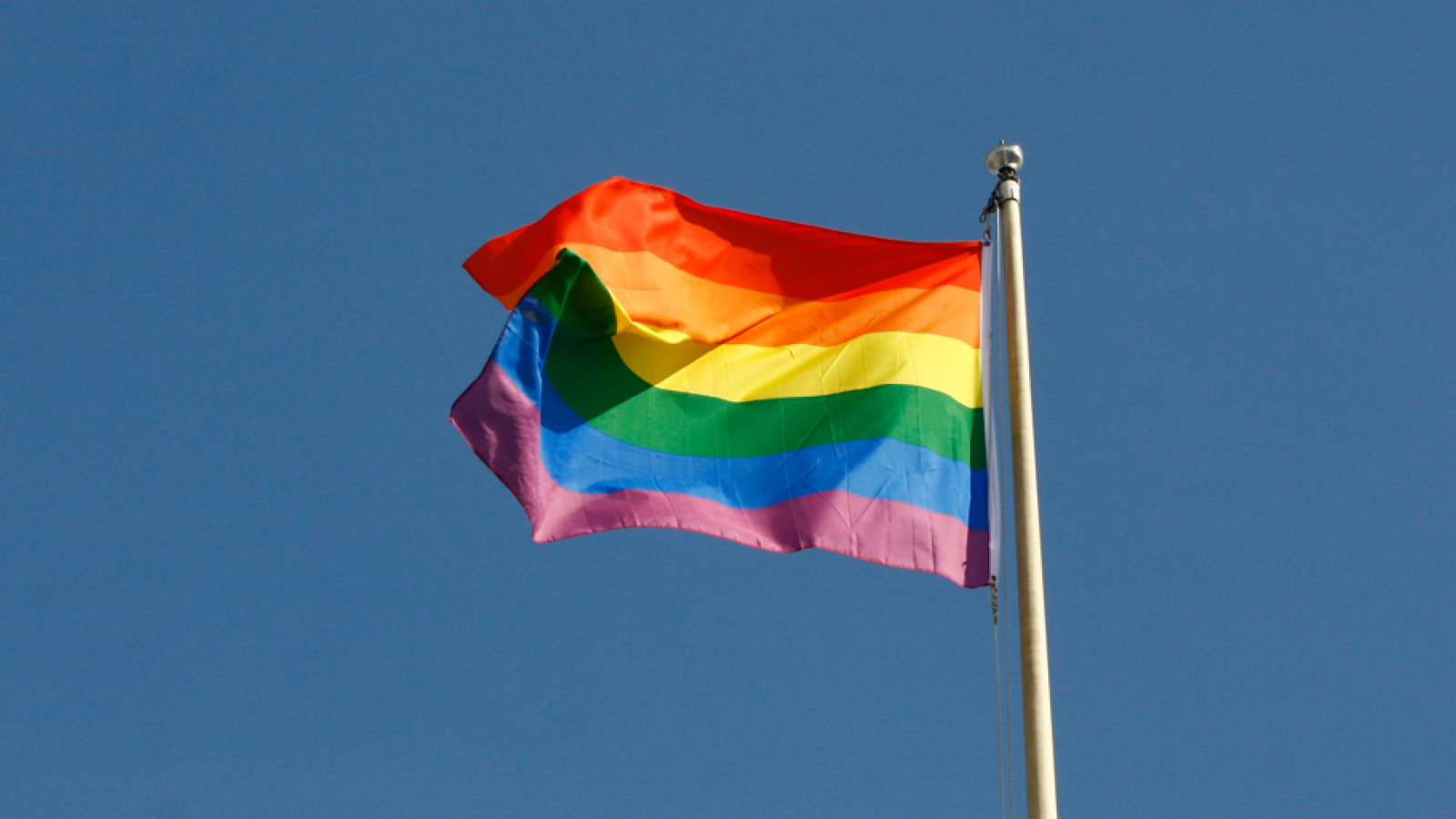 Rainbow flag waving against a clear blue sky, symbolizing LGBTQ+ pride and diversity.